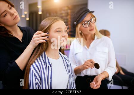 Junge kaukasische Mädchen erhalten Schönheitsverfahren von Make-up-Künstler, geben Ratschläge an Kunden, Blick auf Gesicht auf Spiegel und verwenden dekorative Kosmetik Stockfoto