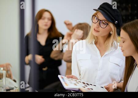Stilvolle moderne blonde Friseur halten Farbpalette in den Händen und zeigen, Beratung für junge Kunden, welche Farbe für ihr Gesicht geeignet ist, in b isoliert Stockfoto