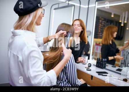 Professionelle Friseur Herstellung Frisur zu jungen kaukasischen Mädchen mit langen Haaren, sorgfältige Friseur und junge schöne Client in Beauty-Salon Stockfoto