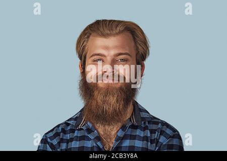 Nahaufnahme Porträt glücklich jungen Mann. Hipster männlich mit Bart in blau kariert kariertes Hemd isoliert auf blauem Studio Hintergrund. Negativer Gesichtsausdruck, Stockfoto