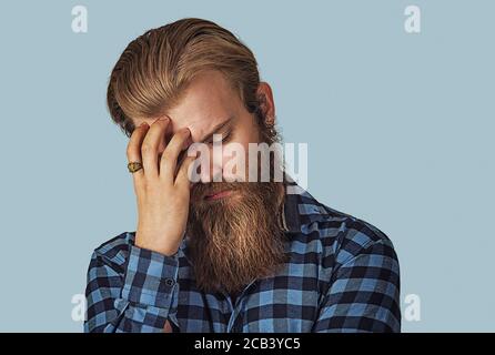 Porträt des deprimierten bärtigen Mannes mit der Hand auf dem Kopf, der an Kopfschmerzen leidet. Hipster Männchen mit Bart in blau kariert Hemd isoliert auf Stockfoto