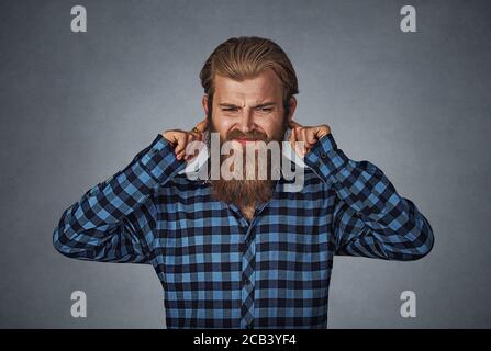 Kopfschuss unzufrieden Mann verstopft Ohren mit Fingern will nicht hören. Hipster Männchen mit Bart in blau kariert kariertes Hemd isoliert auf grau gr Stockfoto