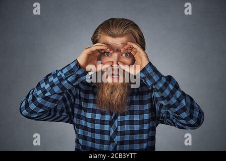 Nahaufnahme Portrait junger, betäubter neugieriger Mann, der wie ein Fernglas durch die Finger schaut und etwas Zukunftsprognose sucht. Hipster Männchen mit Ba Stockfoto