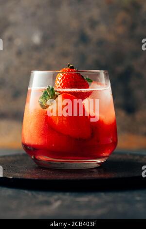 Köstlicher Erdbeer-Cocktail. Frischer Sommercocktail mit natürlichen Erdbeeren und Eiswürfeln. Glas Erdbeersoda auf grunge dunklem Hintergrund. Stockfoto