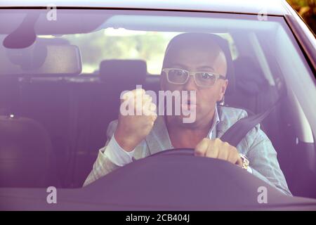 Windschutzscheibe Blick auf einen wütenden Fahrer Mann, zeigt Faust, fluchend. Negative menschliche Emotionen Gesichtsausdruck Stockfoto