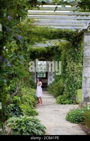 Kleines Mädchen spielt unter der Edwardianischen Pergola, entworfen von Harold Peto, West Dean Gardens, West Sussex Stockfoto