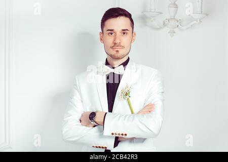 Schöner selbstbewusster junger Mann in schwarzem Hemd und weißer Jacke Auf weißem Hintergrund stehend und auf die Kamera schauend Stockfoto