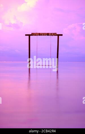 Schaukel am Strand, Koh Rong Samloem, Leng Meng Beach (Saracen Bay) bei Sonnenuntergang. Ein wolkig-violetter Himmel am Abendlicht. Dramatische, mystische Aufnahme. Stockfoto