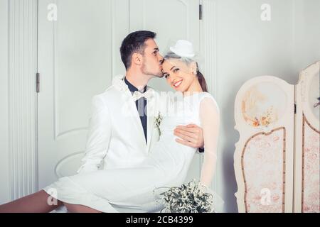 Trendy Mann hält schöne Braut an den Händen und küssen in Stirn im eleganten Interieur stehend Stockfoto