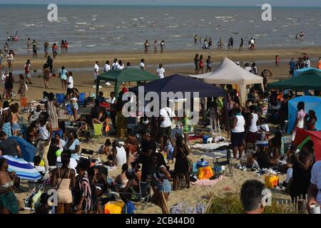 Hunderte steigen am Strand von Camber Sands ab, um den Jahrestag der jamaikanischen Unabhängigkeit zu feiern, der 1962 stattfand. Ängste vor einem zweiten Spike von Covid 19 schienen im Hinterkopf der Menschen zu sein, da soziale Distanzierung manchmal schwierig wurde. Polizeipräsenz Beobachten Sie die Menschenmengen in sicherer Entfernung und erinnern Sie die Menschen daran, möglichst einen sicheren Abstand einzuhalten. Die Veranstalter ermutigten den ganzen Tag über soziale Distanzierungen und baten alle, so sicher und ordentlich wie möglich zu sein. Außerdem spendete sie £750 für die lokale Müllernte, um bei der Müllernte zu helfen Stockfoto