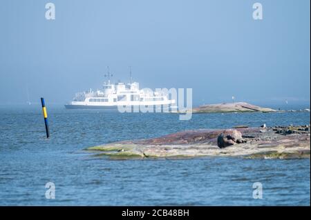 Helsinki / Finnland - 3. Mai 2020: Eine Zugangsfähre, die an einem sonnigen Tag mitten im Nebel über den Horizont fährt. Zwei Skeries im Vordergrund Stockfoto