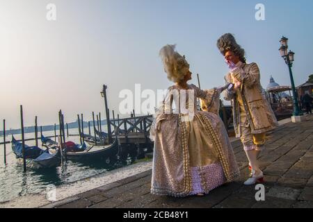 VENEDIG, ITALIEN - 28. JANUAR 2018: Ein Mann und eine Frau mit einem typischen venezianischen Kostüm, während des Karnevals von Venedig mit San Marco Platz im Hintergrund Stockfoto