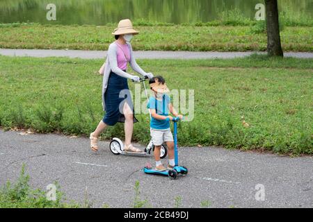 Eine asiatisch-amerikanische Mutter und Sohn reiten Roller, während sie chirurgische Masken tragen. In Queens, NYC. Stockfoto