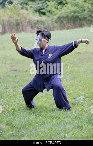 Eine chinesisch-amerikanische Frau mit Gesichtsschutz nimmt an einer Tai Chi-Klasse/Lektion im Kissena Park in Flushing, New York City Teil. Stockfoto