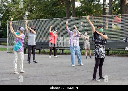 Frauen verschiedener Altersgruppen und Ethnien besuchen einen Tai Chi-Kurs am Morgen mit chirurgischen Masken und sozialer Distanzierung. In Queens, New York City. Stockfoto