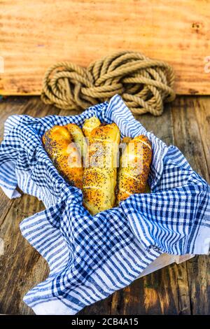 In Teig gebackene Würstchen, mit Salz und Mohn bestreut in einem rustikalen Korb. Würstchenbrötchen, köstliche hausgemachte Backwaren in einer rustikalen Komposition. Stockfoto