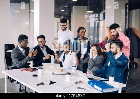 Mixed-Race Gruppe von neun verschiedenen glückliche Menschen stehen rund um die Tabelle mit den Kollegen sitzen, applaudieren Team Leistungen Stockfoto