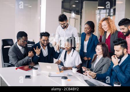 Mixed-Race Gruppe von neun verschiedenen glückliche Menschen stehen rund um die Tabelle mit den Kollegen sitzen, applaudieren Team Leistungen Stockfoto