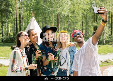 Lächelnd schöner afroamerikanischer Kerl in Sonnenbrille posiert mit besten multi-ethnischen Freunde auf dem Campingplatz beim Selfie zusammen Stockfoto