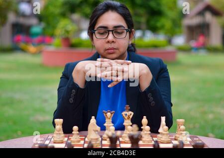 Ein indisches Mädchen, das Schach spielt, wartet darauf, dass die Gegnerin spielt und ängstlich über ihren nächsten Zug nachdenkt. Konzept - Idee, Strategie Stockfoto