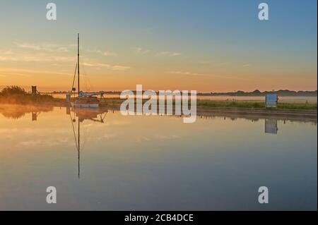 Potter Heigham, Norfolk Broads und ein Segelboot, das während eines nebligen Sommersonnenaufgangs auf dem Fluss Thurne festgemacht wurde. Stockfoto