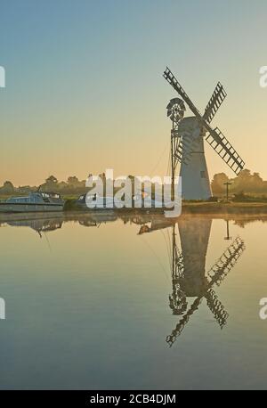 Thurne Dyke Entwässerung Windmühle Norfolk, spiegelt sich in der Fluss Thurne bei Sonnenaufgang mit Booten am Flussufer festgemacht. Stockfoto
