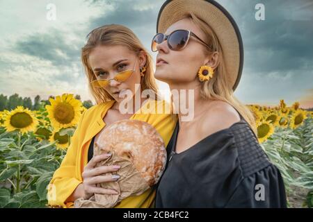 Zwei stilvolle Mädchen posieren in einem Sonnenblumenfeld bei Sonnenuntergang. Stockfoto