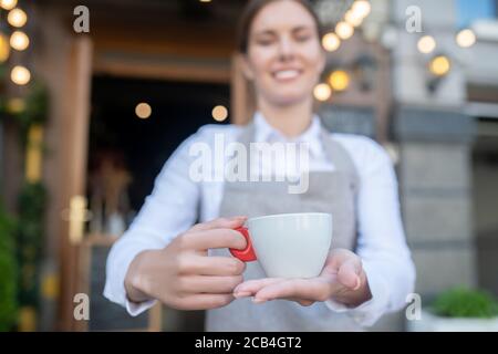 Nette Kellnerin in grauer Schürze mit einer Tasse Kaffee Stockfoto