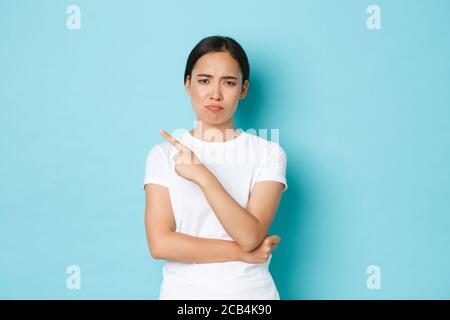 Skeptisch und unzufrieden, grimacing asiatische Mädchen suchen enttäuscht oder unzufrieden mit Promo-Angebot, Zeigefinger oben links Ecke, beschweren Stockfoto