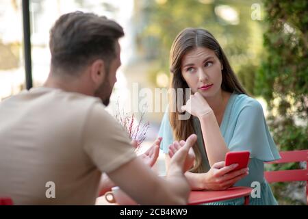 Paar mit Missverständnis im Open-Air-Café, traurige Frau hält ihr Telefon Stockfoto