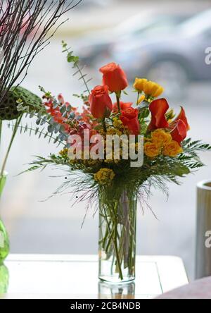 Blumenarrangement in einer klaren Glasvase mit Rosen, Calla Lilien und anderen hellen Blumen. Stockfoto