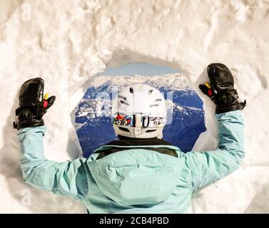 Hinter einer erwachsenen Skifahrerin, die durch ein Loch in der Schneewand auf die weitläufige Bergaussicht blickt. Kontemplation. Winter. Mit Kopierbereich. Stockfoto