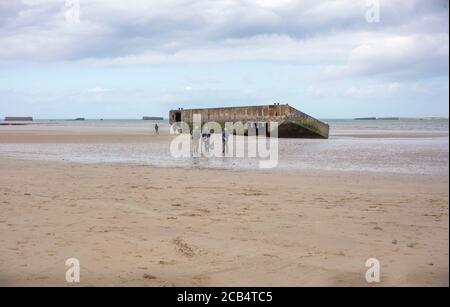 Männer am Strand schauen auf Überreste von Mulberry Häfen und blockieren Schiffe von D-Day Landungen in Arromanches-les-Bains, Normandie, Frankreich Stockfoto