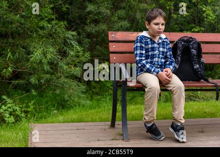 Trauriger Schuljunge mit Rucksack auf einer Straßenbank sitzend Und denken Stockfoto