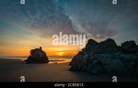 Die Menschen sitzen auf Felsen und beobachten den dramatischen Sonnenuntergang an der Küste von Oregon. Stockfoto