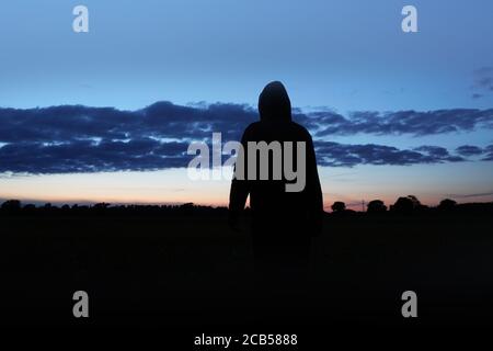 Eine geheimnisvolle Kapuzenfigur, zurück zur Kamera. Silhouetten, Blick auf den Sonnenuntergang. Stockfoto