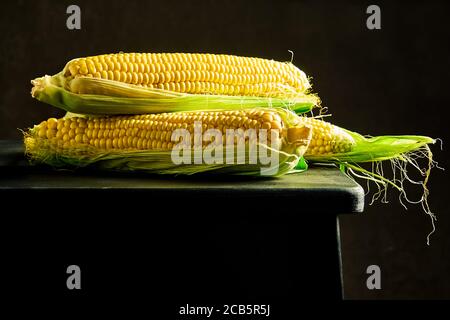 Cobs von reifen rohen Mais auf einem dunklen Holztisch. Gesundes Essen, frische rohe Maiskolben, rustikalen Stil Stockfoto