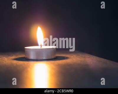 Einzelne Teelicht Kerze auf dem weichen verschwommenen grauen Hintergrund Stockfoto