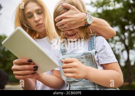 Ernsthaft weiblich, die Hand auf die Augen des kleinen Mädchens legt Stockfoto