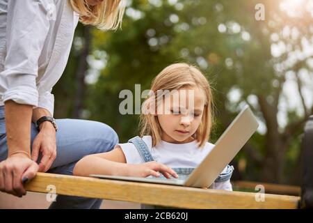 Aufrichtige kleine Mädchen mit Laptop im Park Stockfoto