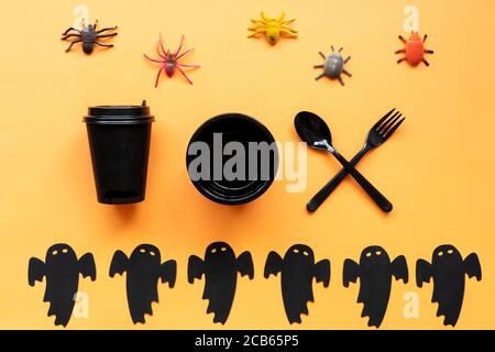 Flacher Halloween Hintergrund mit schwarzem Geschirr, dekorativen Spinnen und Gespenst auf orangefarbenem Hintergrund. Platz für Text kopieren. Einladung zum festlichen Abendessen. Stockfoto