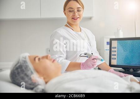 Kosmetikerin sitzt bei ihrem Klienten während des kosmetischen Eingriffs Stockfoto