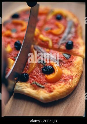 Schneiden einer hausgemachten Pizza auf Tomatenbasis mit Oliven, Paprika, Basilikum und Sardellen Belag gekrönt Stockfoto