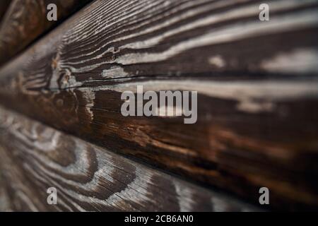 Rustikale Textur an der Wand im Freien, Seitenansicht, dunkler Hintergrund. Selektiver Fokus von braunen alten Volumen rauen Holzplanken, erstaunliche natürliche Muster für Design und Dekoration. Konzept der natürlichen Einrichtung. Stockfoto