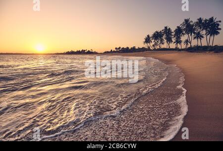 Tropischer Strand bei Sonnenuntergang mit Sonne im Wasser reflektiert, Farbtonung angewendet. Stockfoto