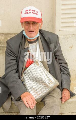 Obdachloser Mann mit einem Gesichtsschutz um sein Kinn und einer Baseballmütze "Margate is great again" in Ramsgate High Street, Thanet, Kent, England, Großbritannien. Stockfoto