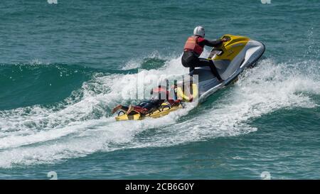 Ein Panoramabild von RNLI Rettungsschwimmern im Dienst beim Fahren eines Jetski am Fistral in Newquay in Cornwall Stockfoto