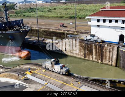 Der Bug des Containerschiffes Hansa Europe in die Miraflores Schleuse auf dem Panamakanal, Panama, niedrige Wasserseite durch elektrische Maultierschlepper geführt. Stockfoto