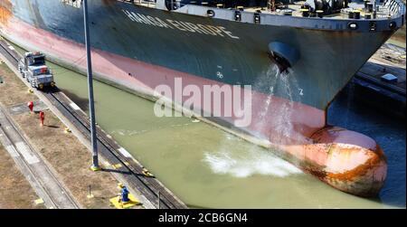 Der Bug des Containerschiffes Hansa Europe in die Miraflores Schleuse auf dem Panamakanal, Panama, niedrige Wasserseite durch elektrischen Schlepper und Entlüftungswasser geführt Stockfoto