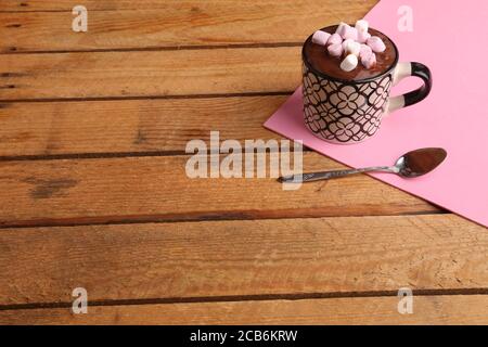 High-Winkel Schuss einer Tasse geschmolzene Schokolade mit Marshmallows auf einem rosa Papier auf einer hölzernen Oberfläche Stockfoto